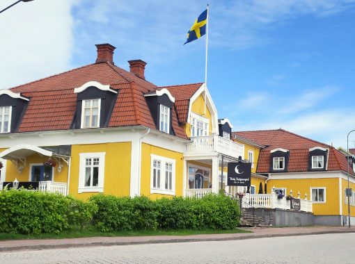 Broby gästgivaregård, hotell med gul träfasad och svenska flaggan hissad.